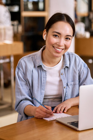 Young smiling Asian woman student elearning online using laptop.の写真素材