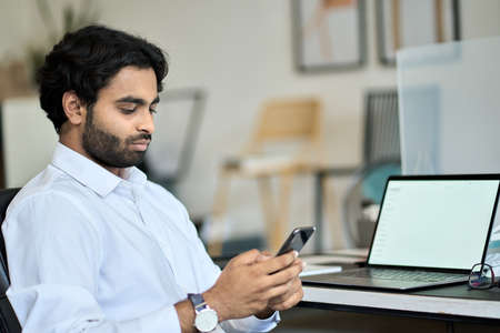 Indian business man employee using smartphone texting at work.