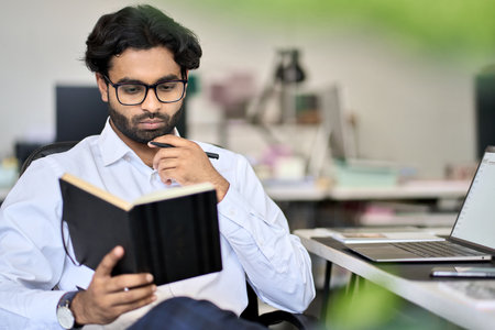 Busy indian male employee planning agenda in notebook working in office.