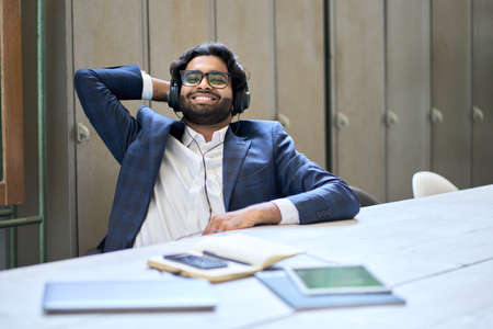 Young happy indian business man wearing headphones sitting at workplace.の写真素材