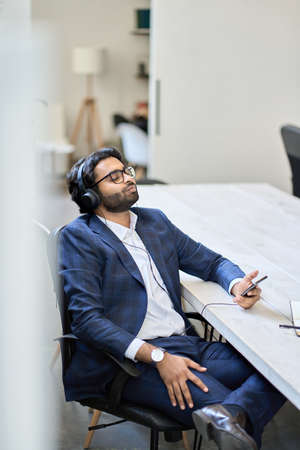 Relaxed indian businessman wearing headphones sitting listening to mobile music.の写真素材
