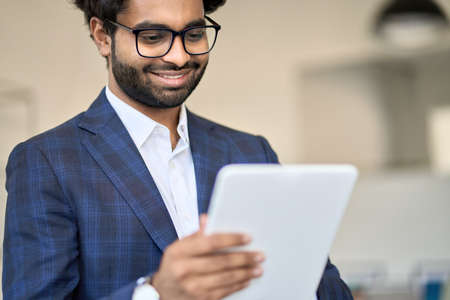 Smiling young indian business manager wearing suit using digital tablet.の写真素材