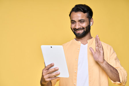 Happy indian man video calling on digital tablet isolated on yellow background.の写真素材