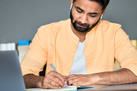 Indian man writing notes while learning online business education course.の写真素材