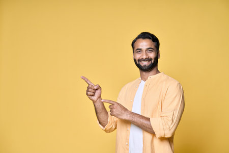 Happy indian man pointing fingers advertising isolated on yellow background.の写真素材