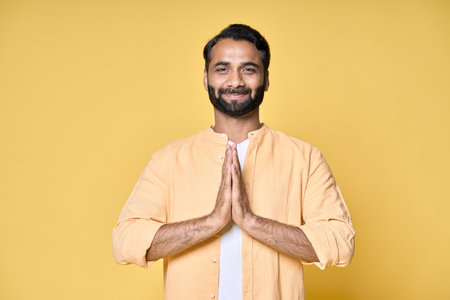 Mindful happy indian man meditating holding hands in namaste isolated on yellow.の写真素材