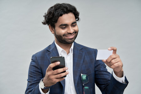 Happy indian arab business man using phone holding credit card.の写真素材