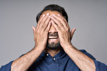 Happy indian man closing eyes with hands isolated on gray background.