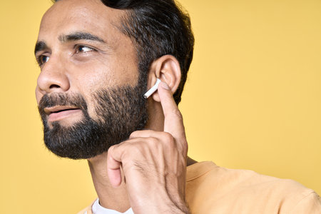 Smiling indian man wearing earbuds listening music or podcast. Closeup
