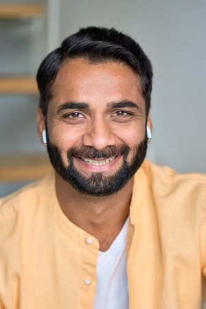 Happy smiling indian man looking at camera indoors. Close up vertical portrait.