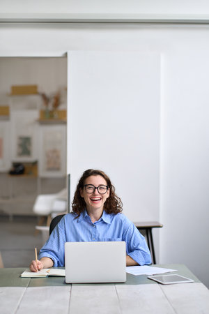 Young cheerful business woman student sitting at office desk with laptop.
