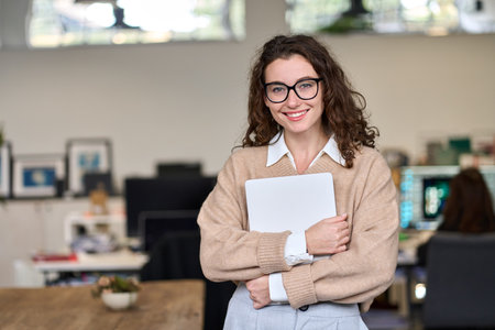Young smiling professional business woman standing in office looking at camera.