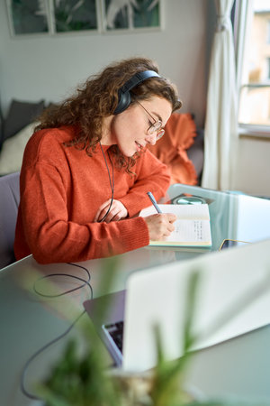 Young woman university student wearing headphones using laptop elearning.