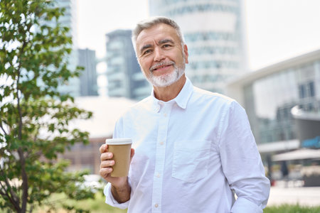 Confident happy mature older business man holding coffee, outdoor portrait.