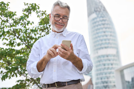 Smiling senior professional businessman holding mobile phone using cell in city.