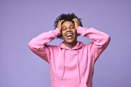 Happy hipster African American teen guy wearing pink hoodie isolated on purple.の写真素材