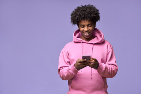 Happy African teen guy holding cell phone using mobile apps isolated on purple.