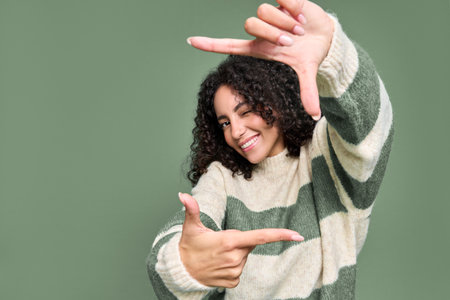 Young happy latin woman having fun pretending making photo isolated on green.の写真素材
