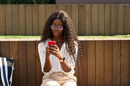 Young pretty African woman student model using mobile phone outdoors.の写真素材