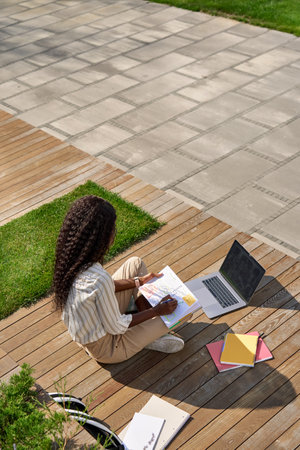 Black young woman student learning using laptop studying outside campus.