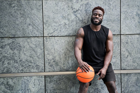 Strong sporty young black man holding basketball ball standing outdoors.の写真素材