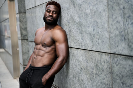 Fit strong shirtless young African black man standing at urban wall.の写真素材