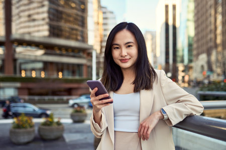 Young Asian business woman professional standing in city holding phone.