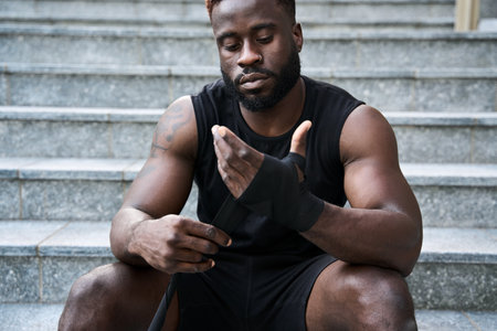 Sporty young black man sitting at urban stairs wrapping hands with boxing tape.の写真素材