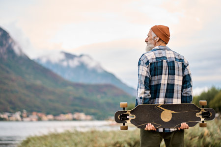 Older hipster man skater standing in nature park holding skate enjoying view.の写真素材