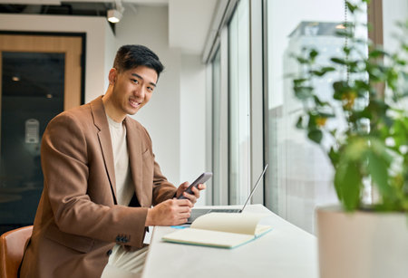Young smiling Japanese business man using cell phone in office.の写真素材