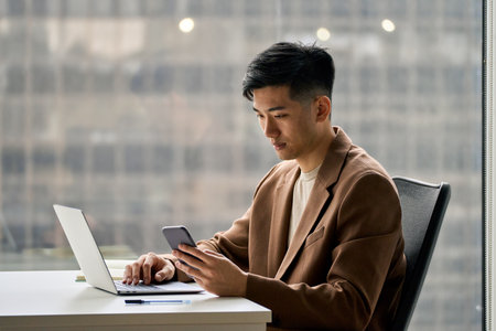 Young serious busy Asian Japanese business man using phone in office.