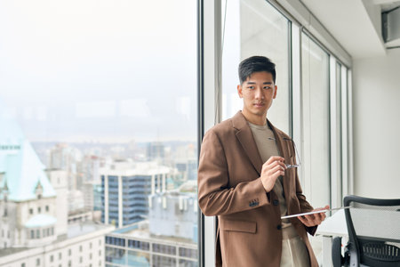 Young Asian business man holding tablet looking at window thinking.