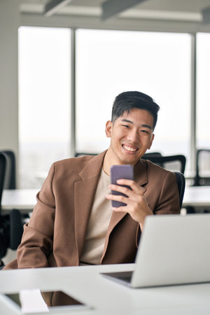 Young happy Asian business man using cell phone in office. Verticalの写真素材