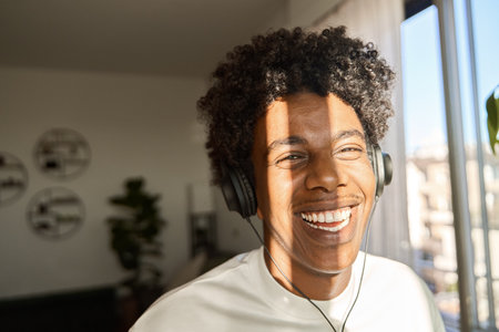 Happy gen z African American guy wearing headphones listening music at home.の写真素材