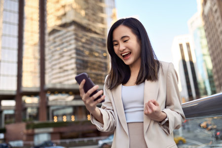 Happy excited young Asian business woman winner holding mobile phone in city.の写真素材
