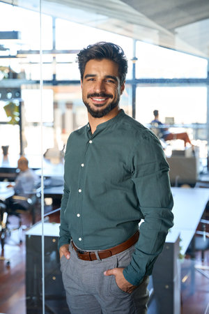 Young happy Latin business man looking at camera in office, vertical portrait.