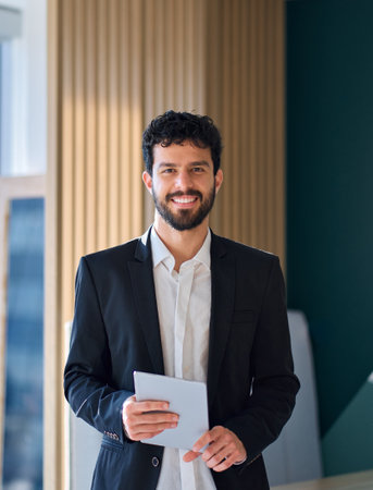 Smiling business man standing in office holding tablet. Vertical portrait.の写真素材