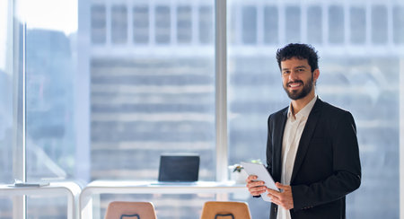 Smiling latin business man standing in office holding tablet, portrait.