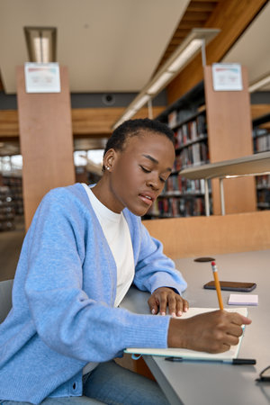 African girl college student writing in paper notebook, taking notes in library.の写真素材