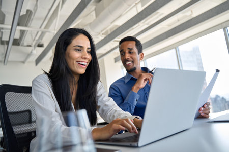 Two happy diverse workers using laptop working on computer at workplace.