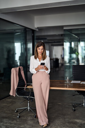 Mid aged business woman holding cellphone using phone in office, vertical.の写真素材