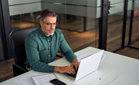 Busy middle aged professional business man working on laptop at office desk.の写真素材