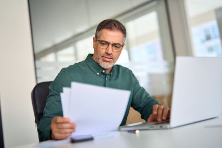 Middle aged business man executive using laptop checking financial documents.