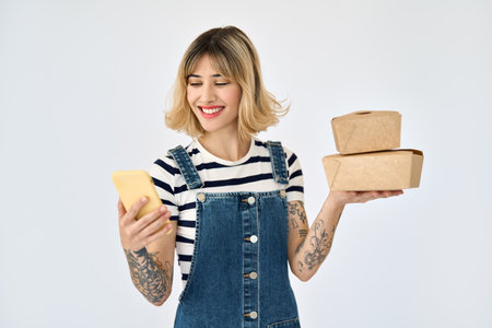 Happy young woman holding phone and food delivery boxes using mobile app.の写真素材