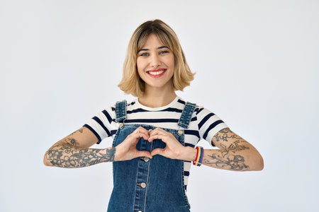Happy gen z young woman with tattoos rainbow bracelet showing heart, isolated.の写真素材