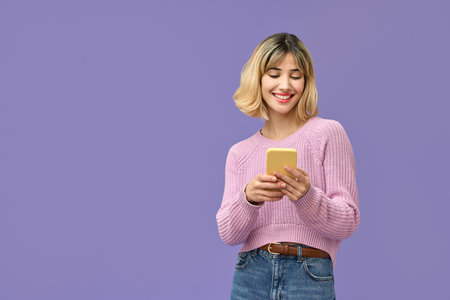 Happy pretty gen z blonde girl using mobile phone isolated on purple background.
