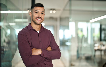 Confident young Latin business man standing arms crossed in office, portrait.の写真素材