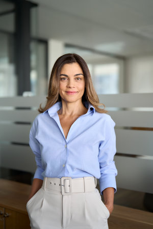 Mature business woman standing in office looking at camera. Vertical portrait.