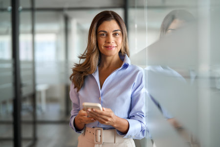 Smiling middle aged woman business investor using phone standing in office.の写真素材