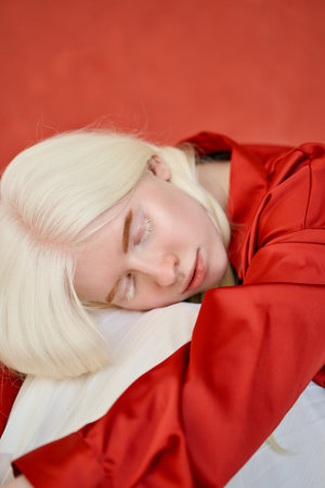 Albino inclusive girl wearing red and white sitting on studio background.